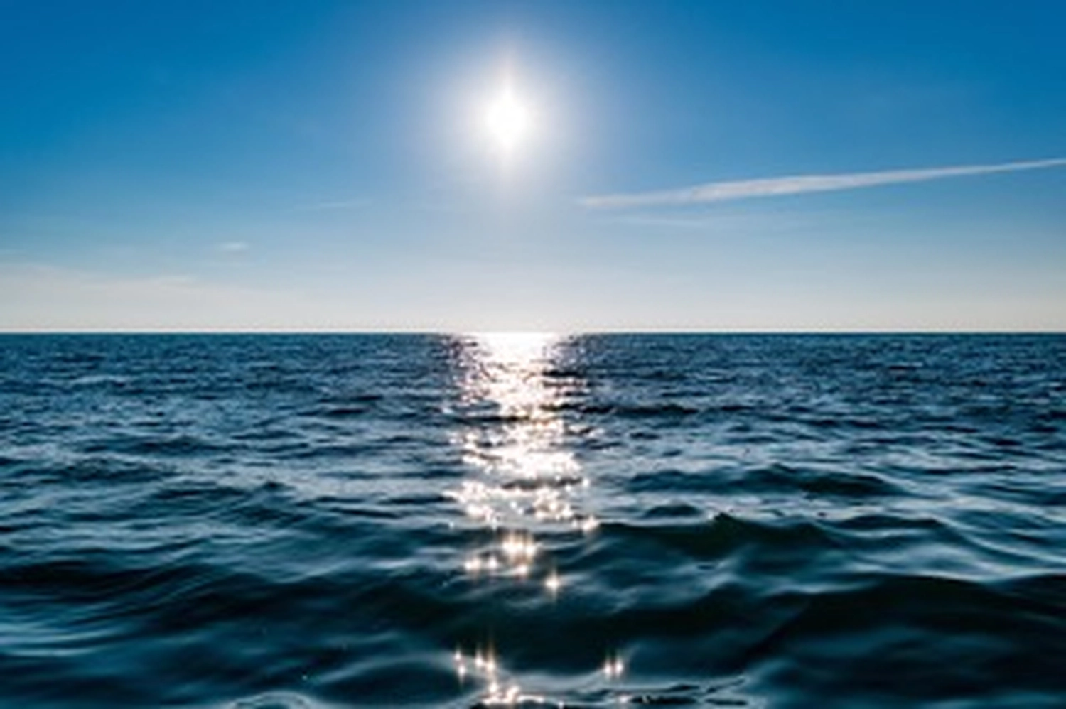 Wirtschaftsverein Apollon - Projektleitung von Konvaleszenz - Eine strahlende Sonne scheint an einem klaren blauen Himmel über einem blauen Ozean und erzeugt eine funkelnde Spiegelung auf der Wasseroberfläche, die sich bis zum Horizont erstreckt.